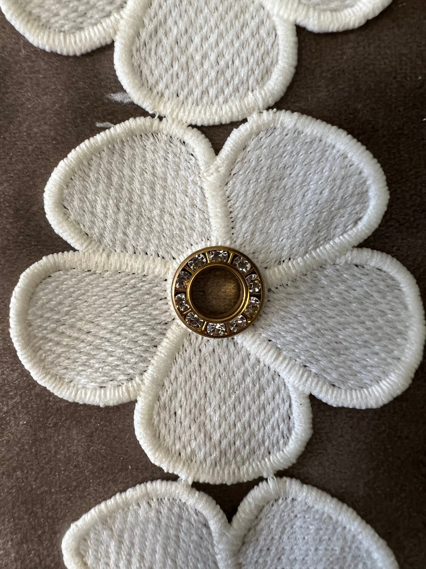 Galon blanc cassé de fleurs percées d'un anneau métallique de strass